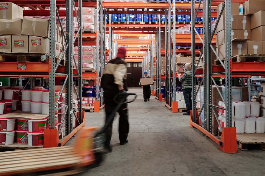 Trabajadores organizando anaqueles en un almacén con cajas y contenedores